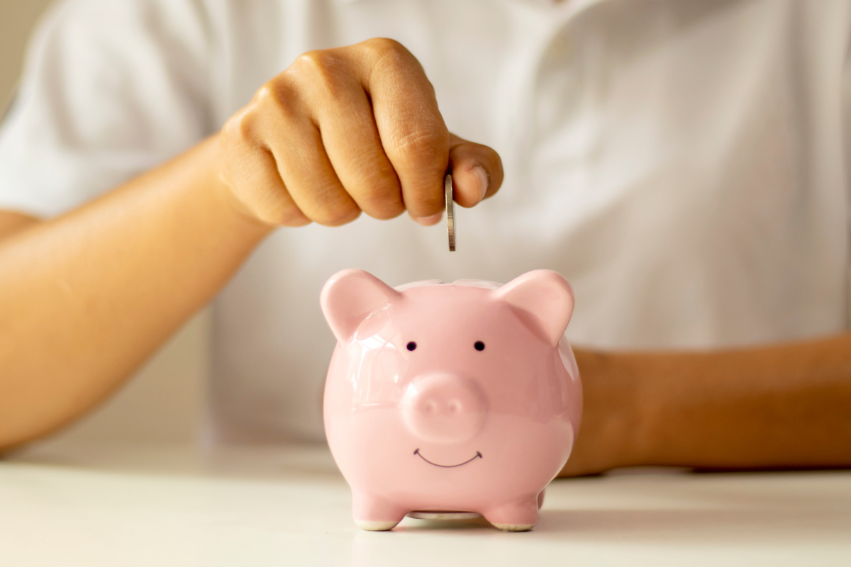 A person in a white T-shirt putting a coin in a pink piggy bank 