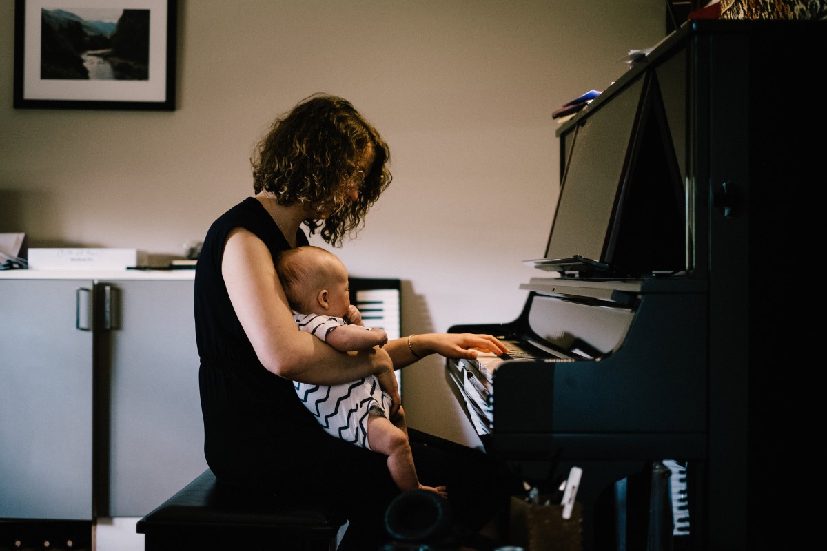Young woman with curly hair sitting at a piano with baby in her lap