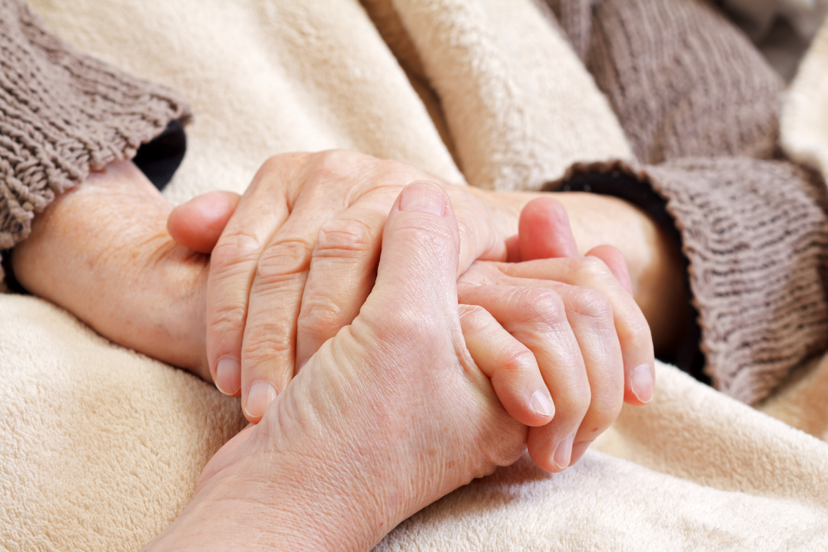 A hand holding the hands of a senior person on a blanket