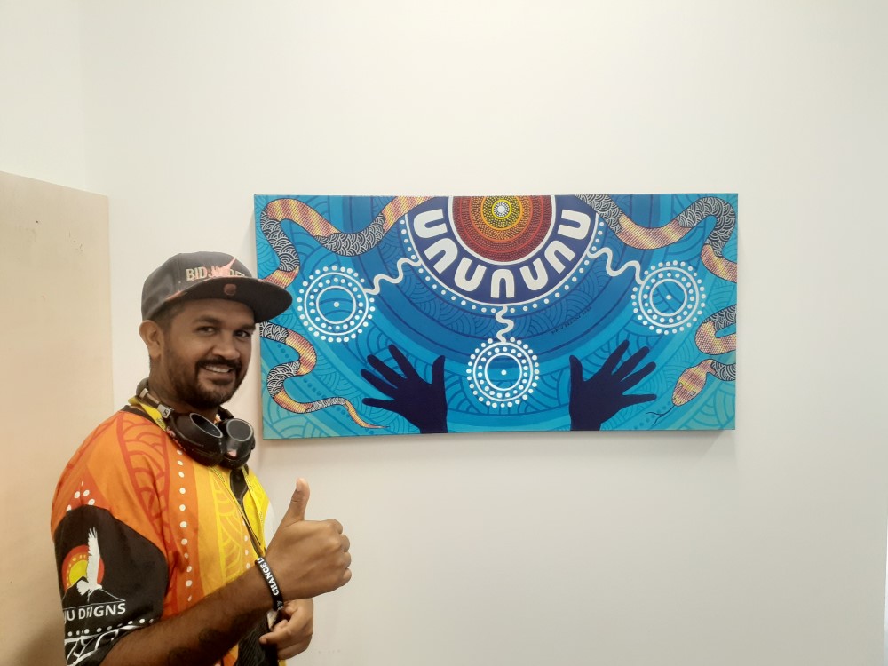 Young Aboriginal man posing with Aboriginal painting on wall