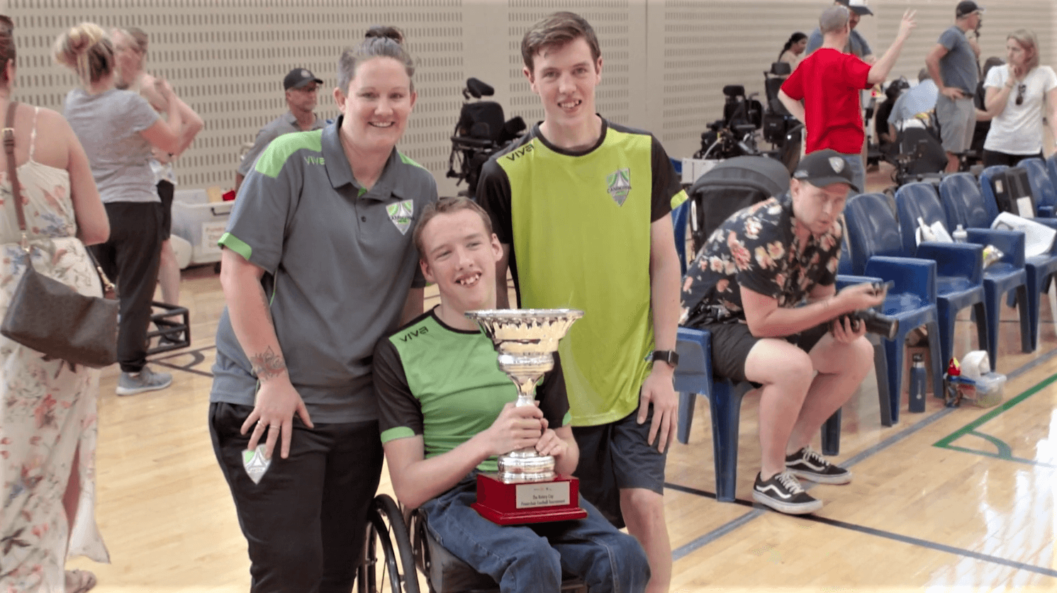 A boy and a woman posing with another boy in a wheelchair, holding a trophy
