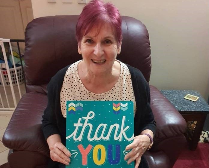 Senior lady sitting in armchair with big thank you card