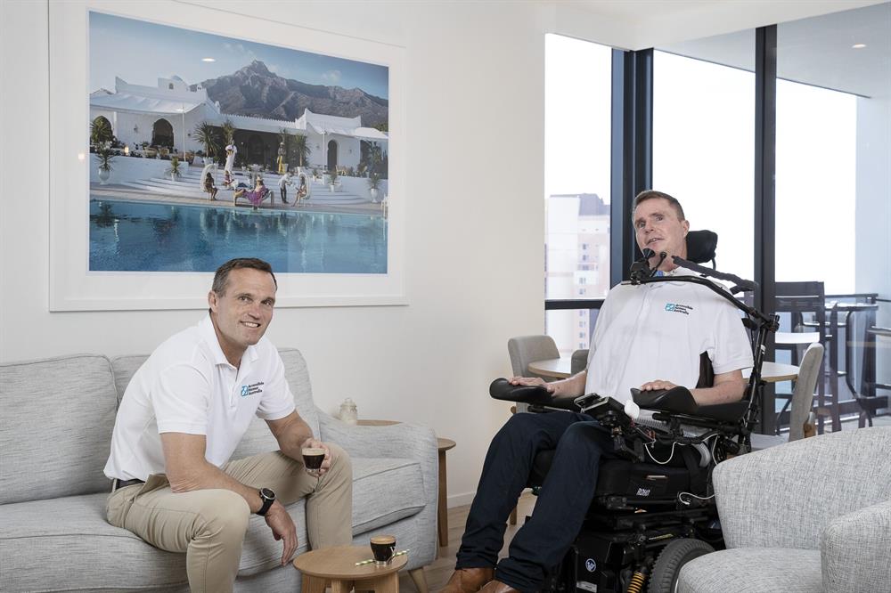 Abled and disabled man sitting in living room, smiling