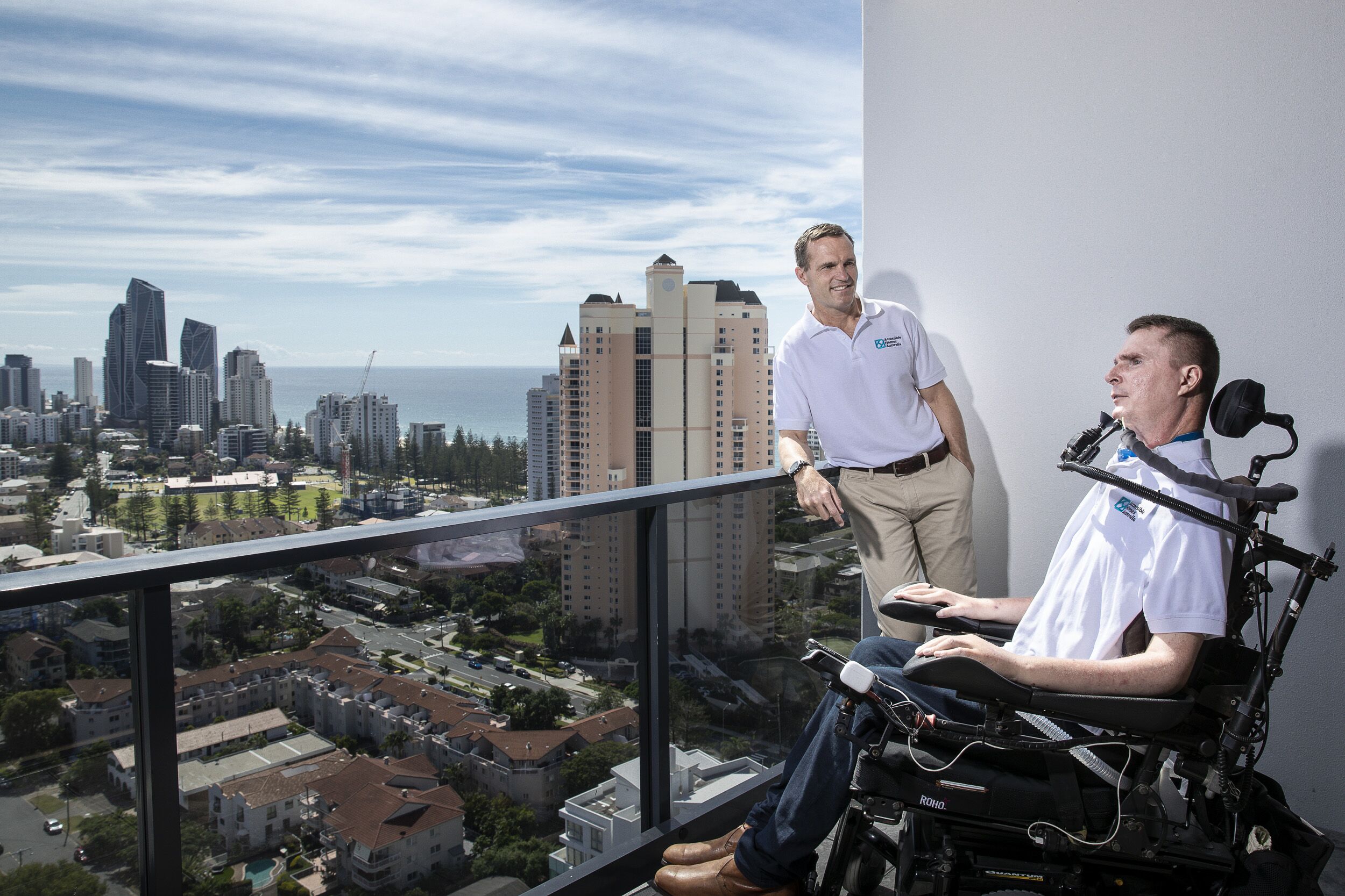 One man standing and one man sitting in a wheelchair on a balcony