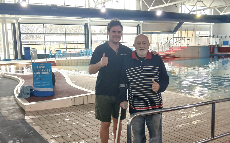 Feros Care Community Support Worker Haydon with beloved client John at the swimming pool. Both are giving the thumbs up!