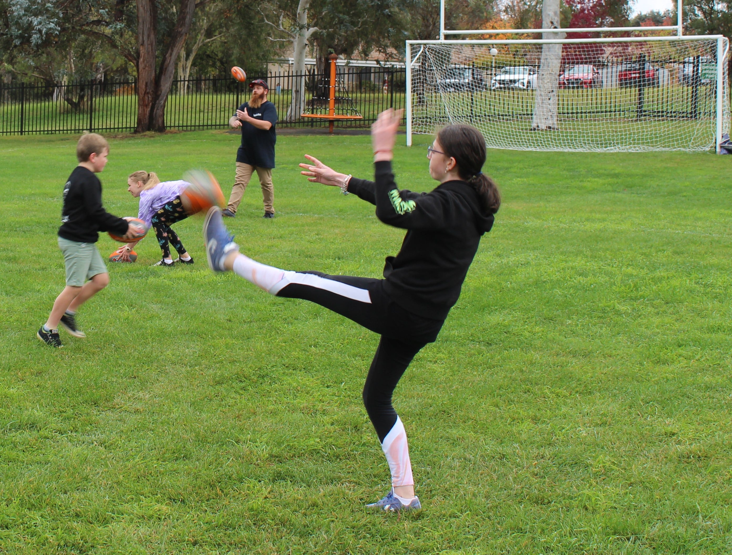Girl kicking ball on outdoor field with others surrounding her