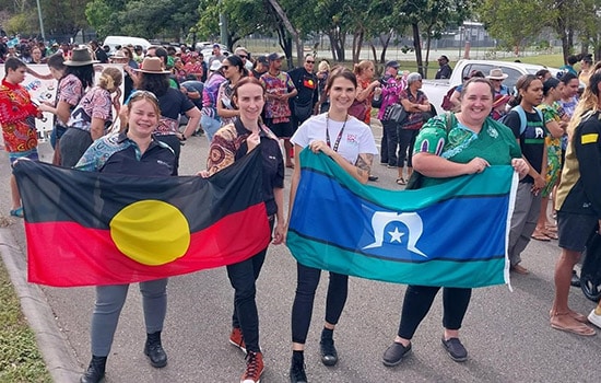 Feros Care Townsville team members holding up Aboriginal and Torres Strait Islander flags at the Townsville NAIDOC Week Big Day Out event.
