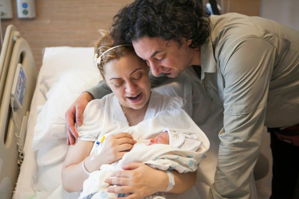 Mother holding newborn baby and husband with arm around his wife