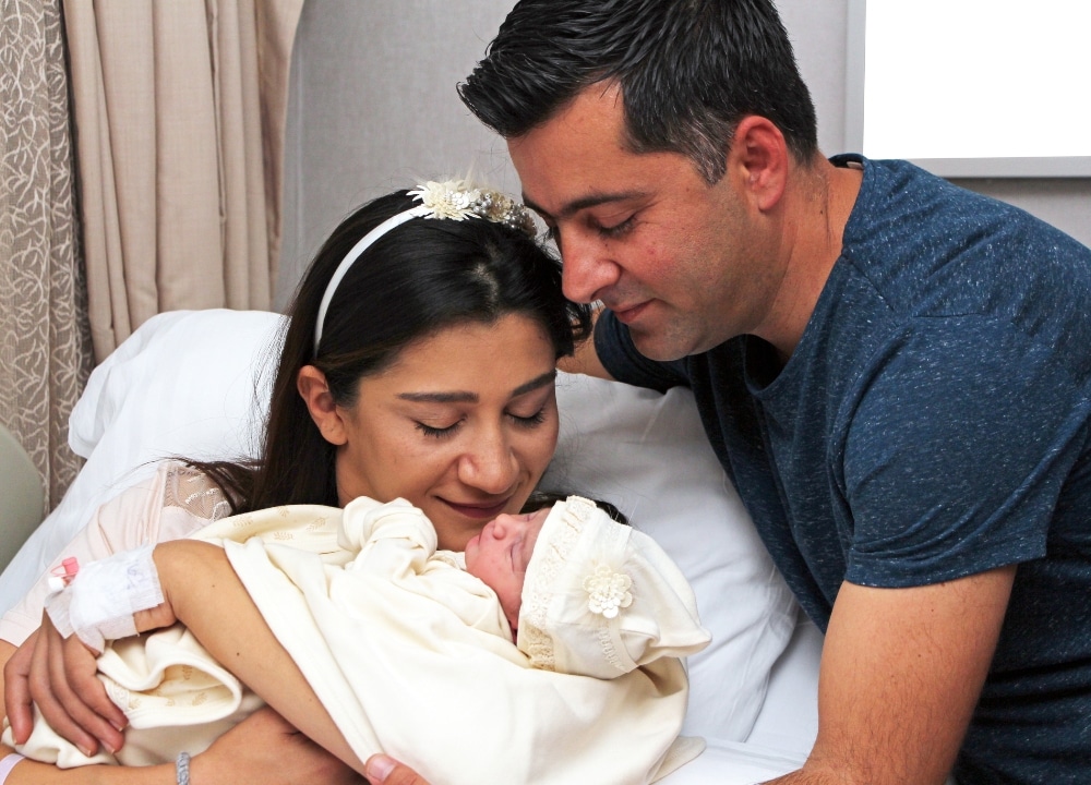 Mother on hospital bed holding newborn baby and father leaning towards them