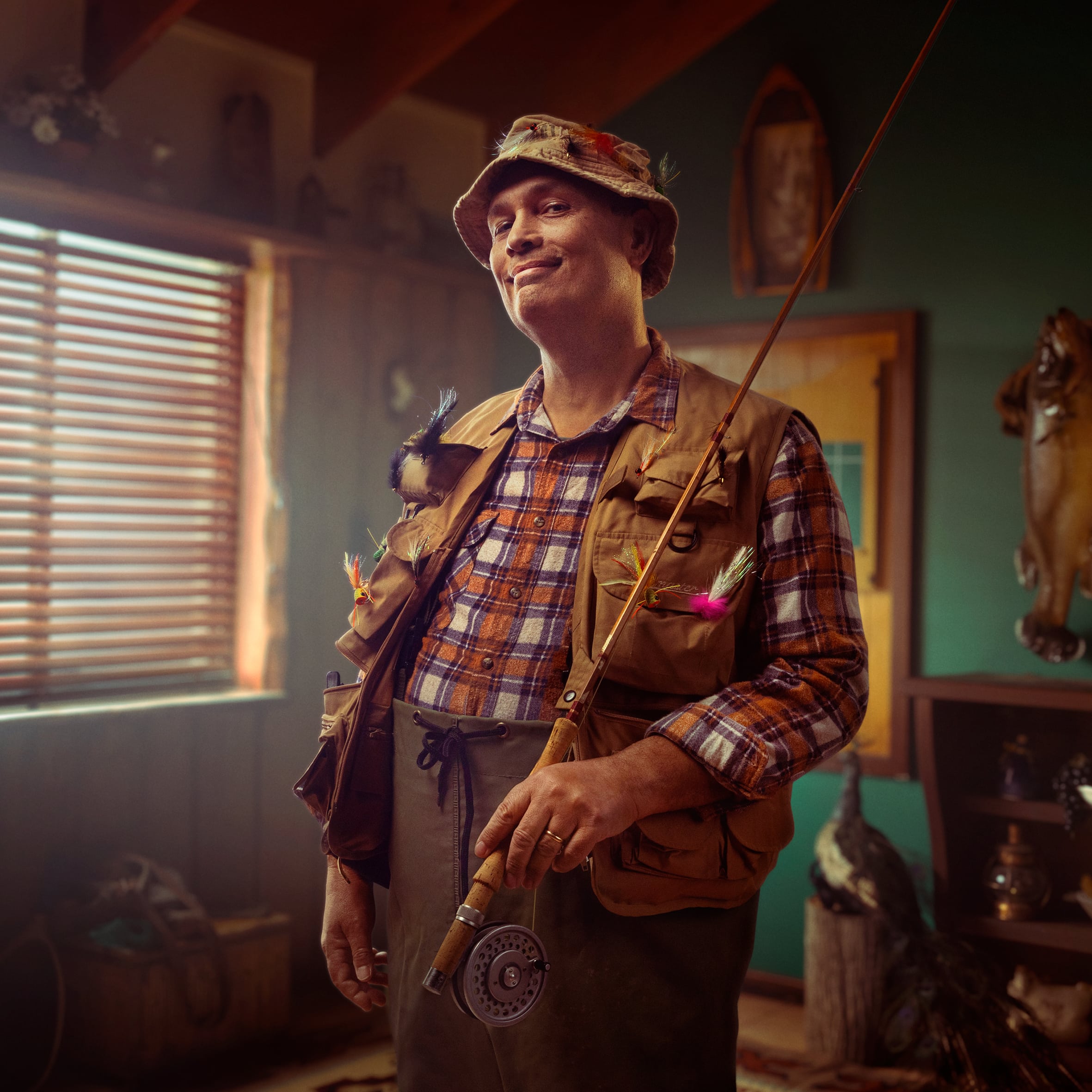 Image of Addiran smiling broadly with fishing attire and a firshing rod in his home