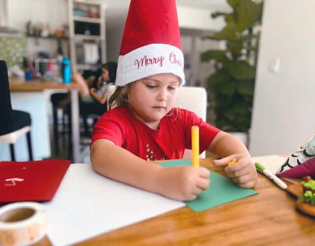 Photo of a child wearing Santa hat and writing a Christmas card