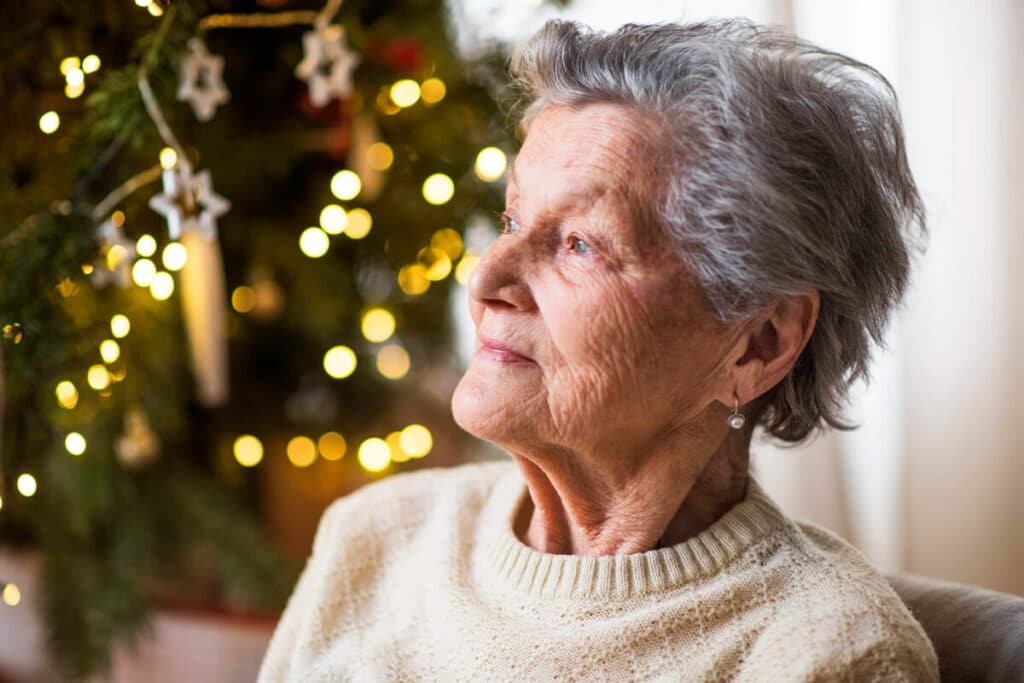 Photo of senior woman in front of a Christmas tree looking sad out the window