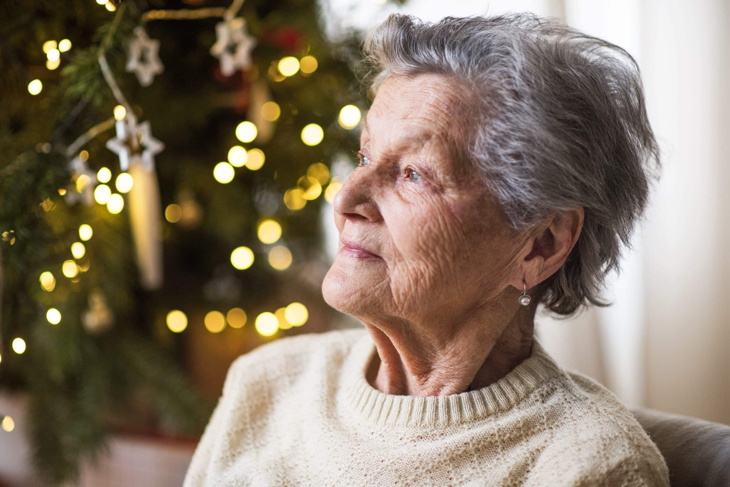 Photo of senior woman in front of a Christmas tree looking sad out the window