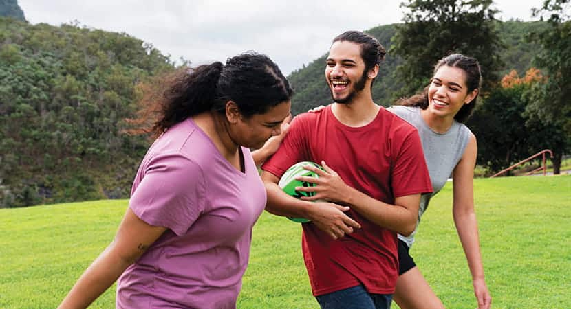 Young adults laughing while running on a field with a football
