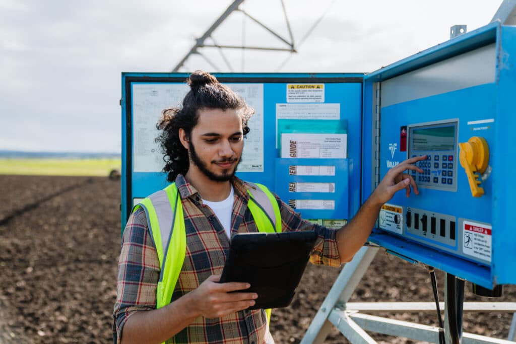 A young man wearing a visibility vest is holding a tablet checking an electrical box