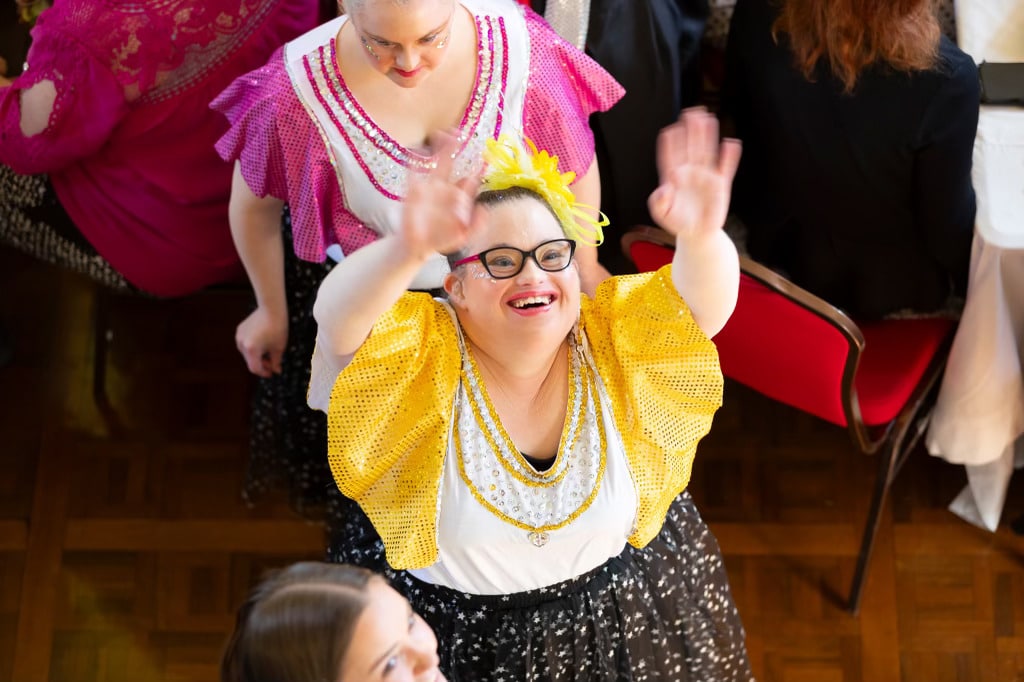 Woman with Down syndrome in dance costume, hands in air, smiling