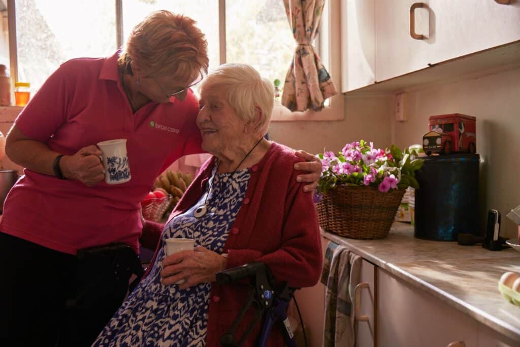 Feros Care Community Support Worker Marion Fleming with her arm around client Diasy sharing a cuppa in the kitchen