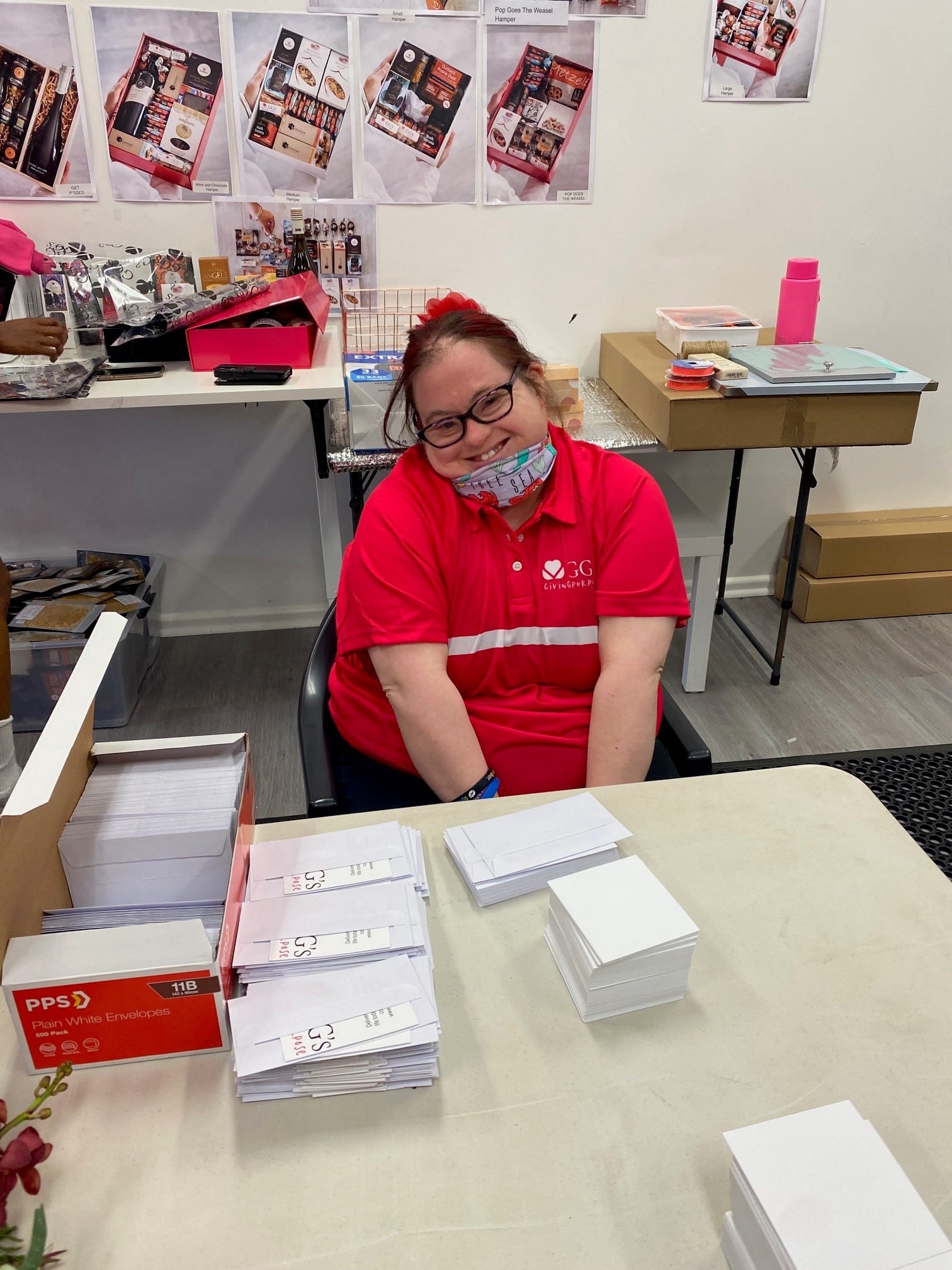 Woman with Down syndrome sitting at desk, wearing a face mask, preparing mail.