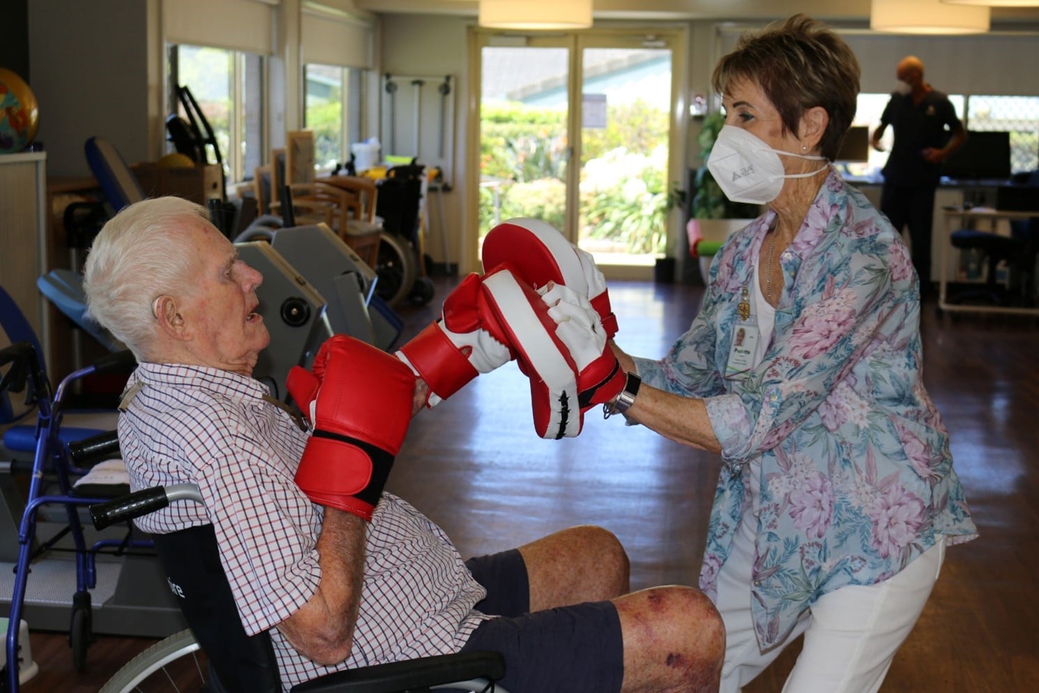 woman in mask dping boxing with old man in wheelchair. physiotherapy centre Feros Care Wommin Bay aged care.