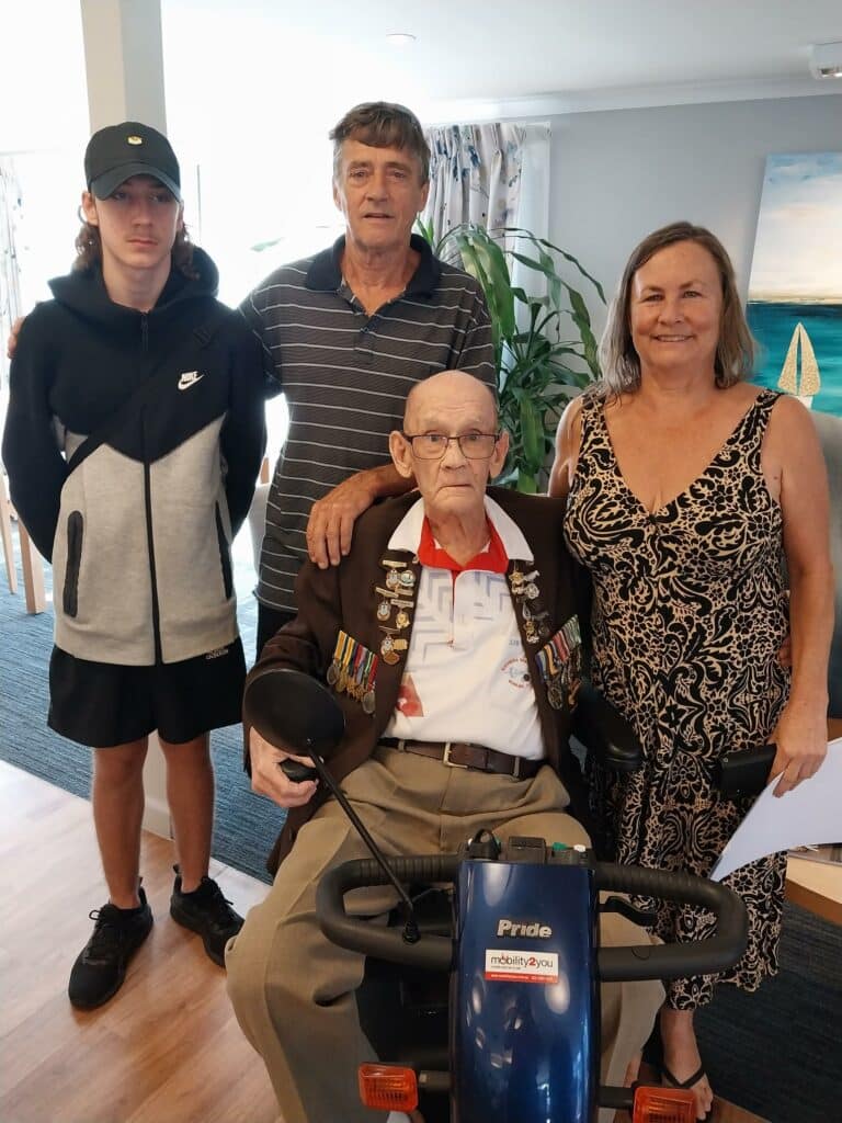 Wommin Bay Village resident and Veteran, John Martin on his mobility scooter surrounded by family. He served in New South Wales, Queensland, Victoria, Papua New Guinea, and twice in Vietnam. x2. 