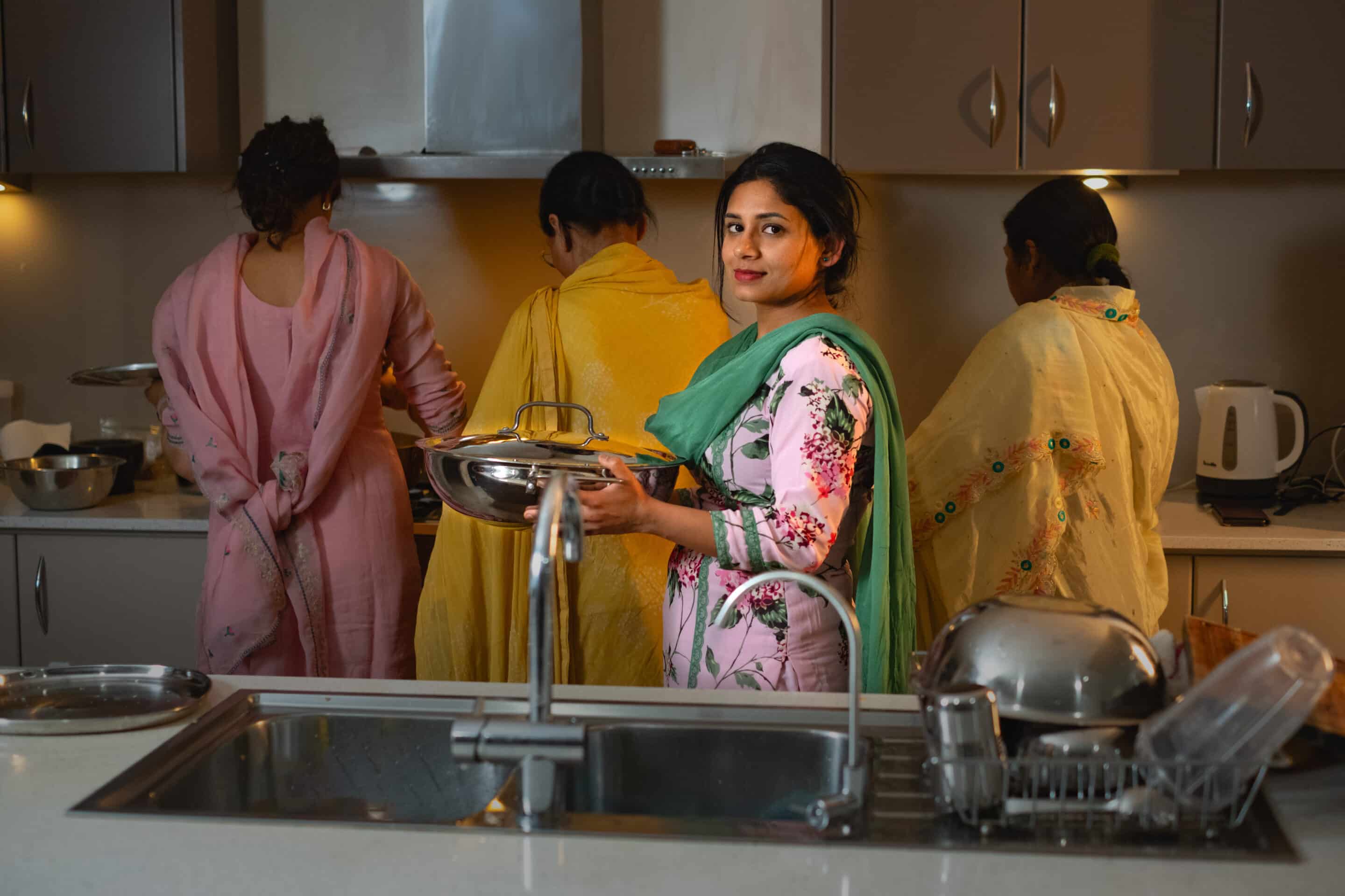 Indian woman in the kitchen in traditional dress, holding a bowl of food.