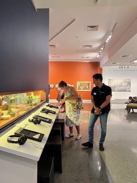 Female Feros Care Social Groups participant looking at an interactive display at Tweed Regional Gallery with a smiling Feros Care Community Support Worker looking on.