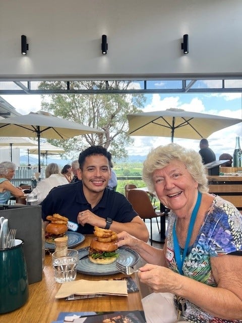 Female Feros Care social groups participant eating a burger and smiling at Tweed Regional Gallery with smiling male Community Support Worker